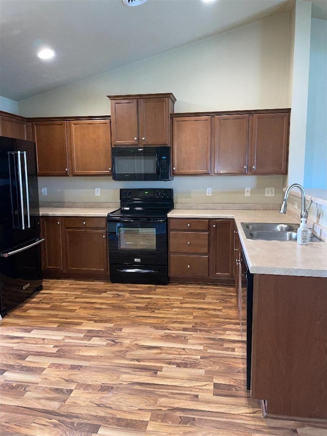 kitchen featuring a sink, light countertops, black appliances, light wood finished floors, and lofted ceiling
