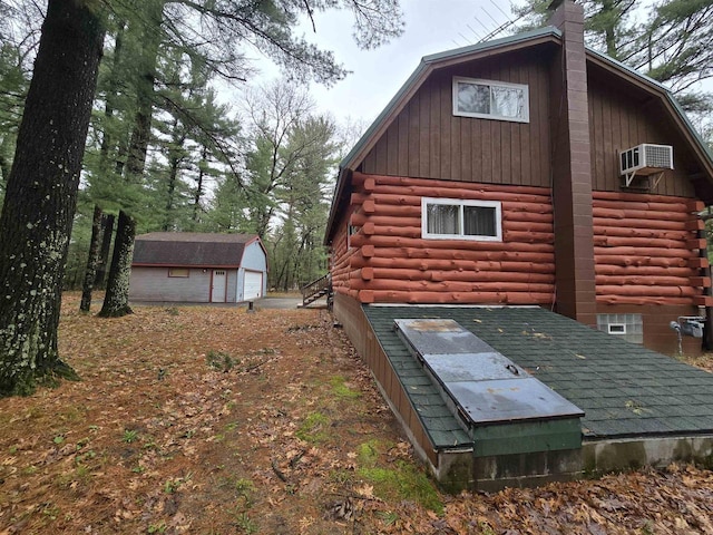 rear view of house with an AC wall unit, a gambrel roof, a chimney, log siding, and an outbuilding
