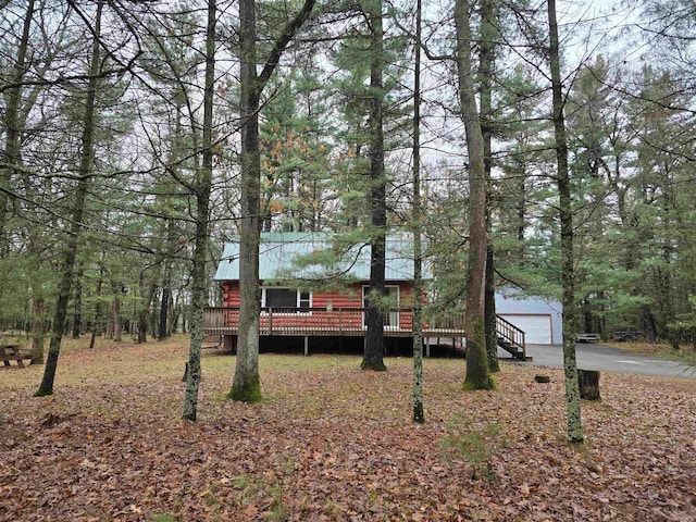 view of front facade with an outbuilding, driveway, a deck, and a forest view