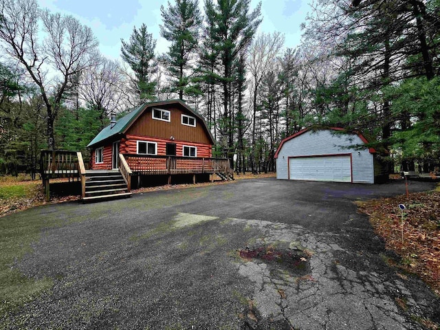 exterior space with an outdoor structure, a garage, a wooden deck, a gambrel roof, and log exterior