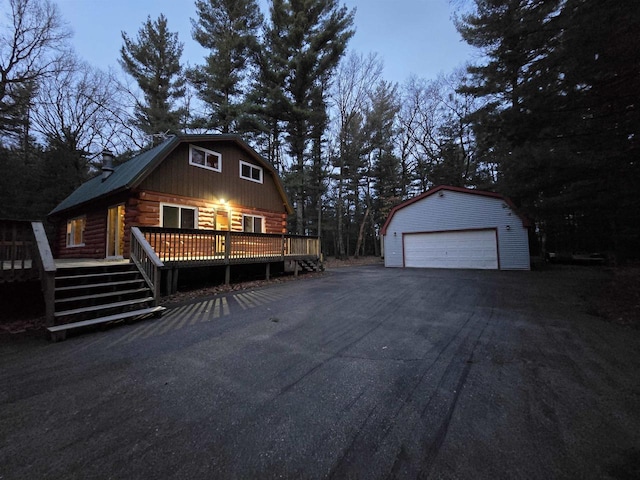 view of front facade with a wooden deck, log siding, a garage, an outdoor structure, and a gambrel roof