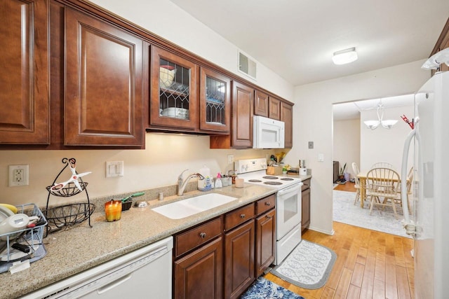 kitchen featuring white appliances, light wood-style floors, light stone counters, a sink, and a notable chandelier