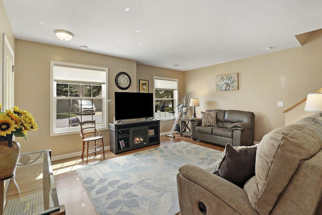 living room with baseboards, wood finished floors, and a warm lit fireplace
