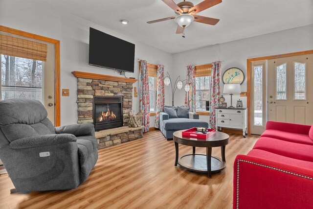 living room featuring a stone fireplace, a ceiling fan, and wood finished floors