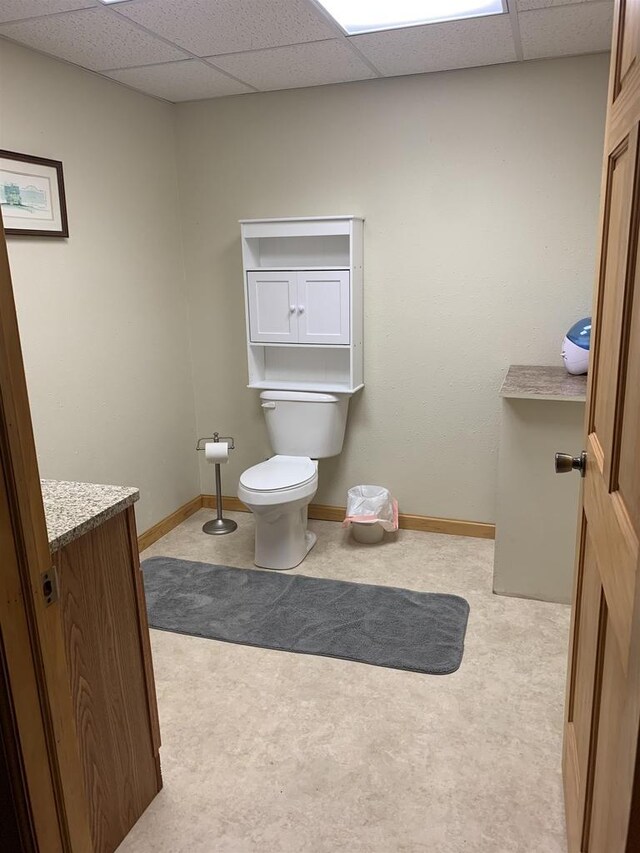 half bathroom with vanity, baseboards, a drop ceiling, and toilet
