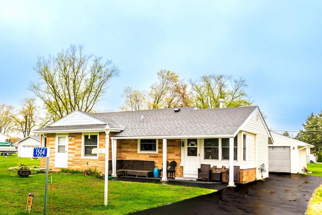 view of front of house featuring roof with shingles, a detached garage, an outdoor structure, a front lawn, and stone siding