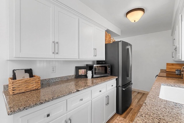 kitchen with white cabinets, light stone countertops, appliances with stainless steel finishes, a sink, and light wood finished floors