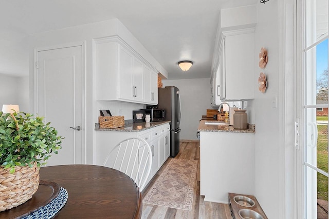 kitchen with a sink, plenty of natural light, light wood-type flooring, and white cabinetry