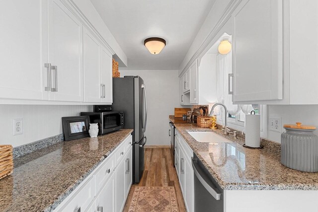 kitchen with appliances with stainless steel finishes, light stone countertops, a sink, white cabinets, and light wood-style flooring