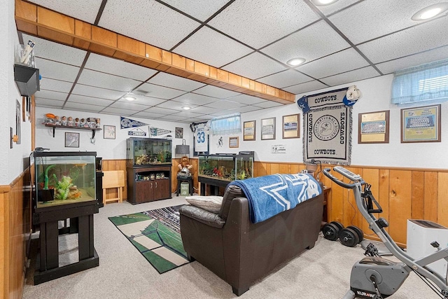 carpeted living area featuring a paneled ceiling, a wainscoted wall, and wooden walls