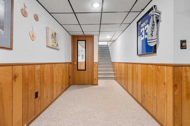 hallway featuring a drop ceiling, a wainscoted wall, wooden walls, and stairway