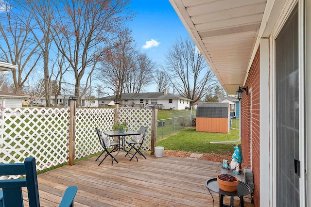 wooden deck with an outdoor structure, a lawn, a fenced backyard, and a storage unit
