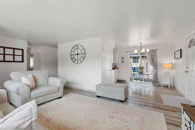 living area with baseboards, a notable chandelier, and light wood-type flooring
