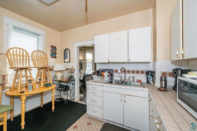kitchen with white cabinets, a sink, tile counters, stainless steel microwave, and tasteful backsplash