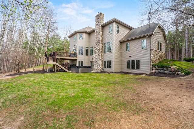 rear view of property with a chimney, a deck, a hot tub, a yard, and stairs