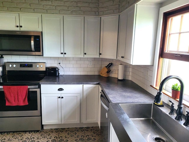 218 7th Ave, New Glarus, WI 53574 - kitchen with white cabinets, dark countertops, a sink, stainless steel appliances, and decorative backsplash