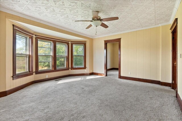 carpeted spare room with crown molding, baseboards, ceiling fan, and an ornate ceiling