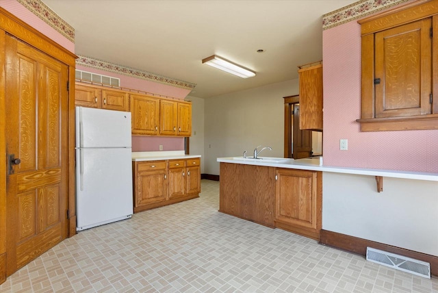 kitchen featuring visible vents, freestanding refrigerator, baseboards, light countertops, and brown cabinets