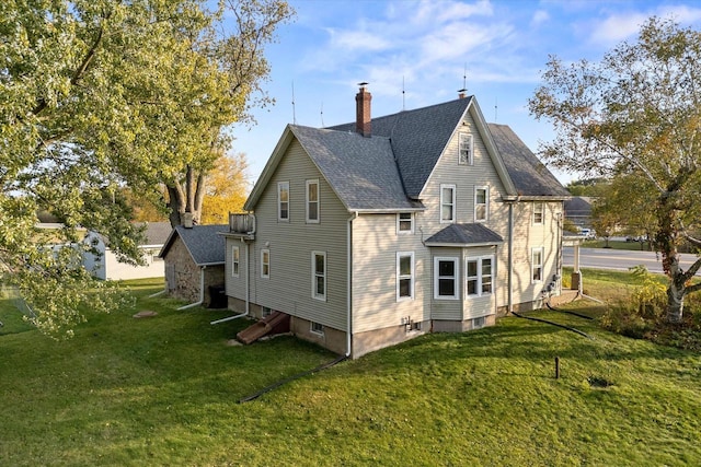 back of property featuring a lawn, a chimney, and roof with shingles