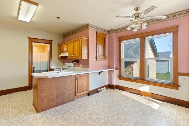 kitchen featuring a sink, light countertops, a peninsula, baseboards, and under cabinet range hood