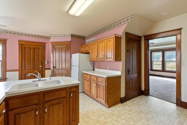 kitchen featuring freestanding refrigerator, brown cabinets, a sink, and light countertops