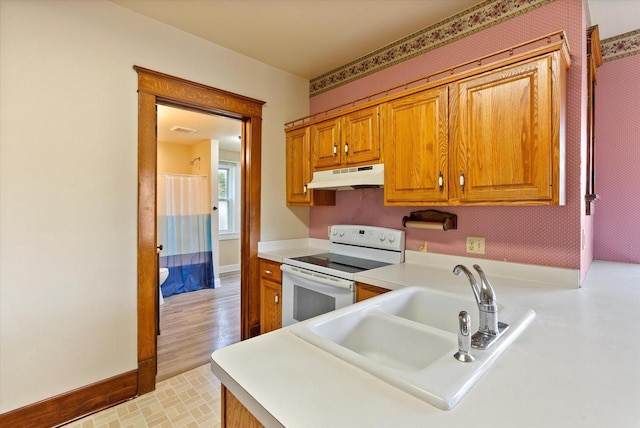 kitchen featuring white electric stove, brown cabinets, a sink, light countertops, and under cabinet range hood