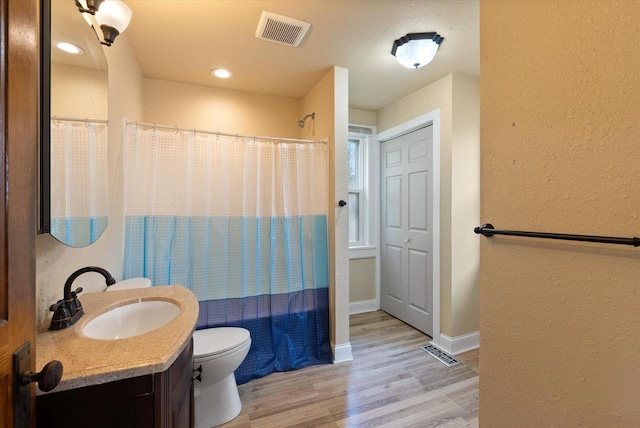 bathroom featuring toilet, a textured wall, visible vents, and wood finished floors