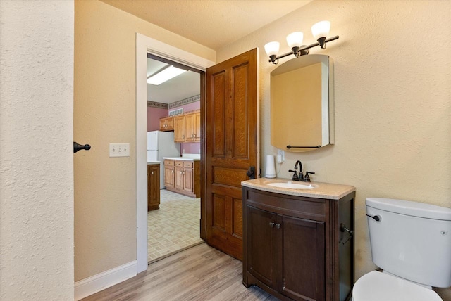 bathroom featuring toilet, a textured wall, wood finished floors, and vanity