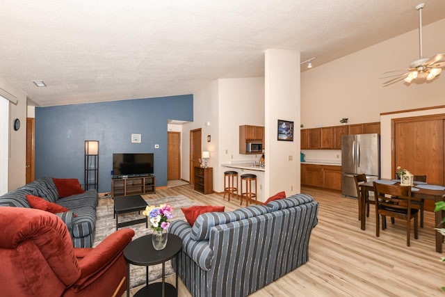 living area with a ceiling fan, light wood-style flooring, a textured ceiling, and high vaulted ceiling