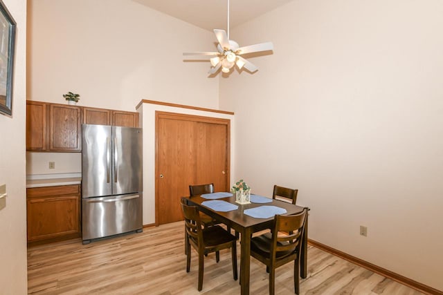 dining area with high vaulted ceiling, ceiling fan, and light wood-style flooring