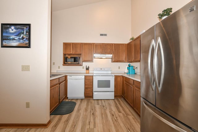 kitchen featuring brown cabinetry, a towering ceiling, appliances with stainless steel finishes, and under cabinet range hood