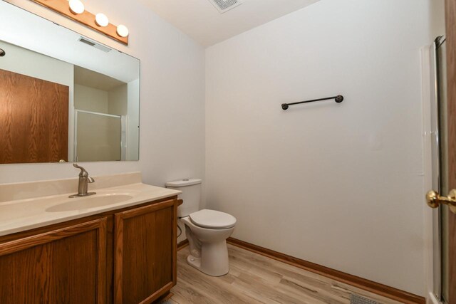 full bathroom featuring vanity, a shower with door, wood finished floors, and visible vents