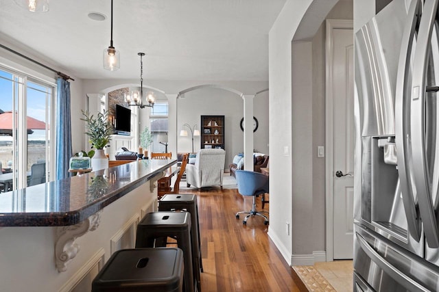 interior space with arched walkways, decorative columns, stainless steel fridge, and a breakfast bar