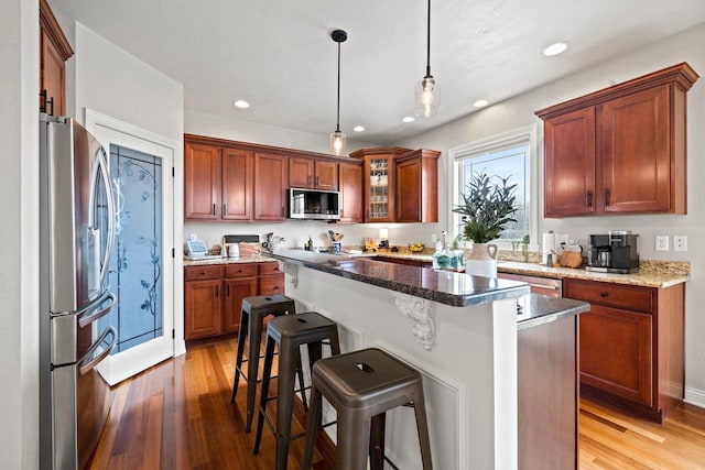 kitchen with a breakfast bar area, decorative light fixtures, appliances with stainless steel finishes, and light wood-style flooring