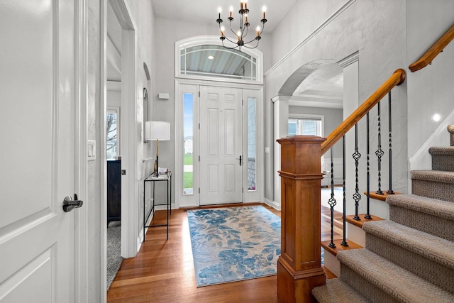 foyer with decorative columns, arched walkways, wood finished floors, an inviting chandelier, and stairs