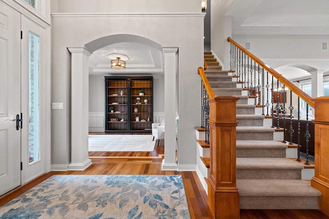 entrance foyer featuring stairs, wood finished floors, ornate columns, a tray ceiling, and arched walkways