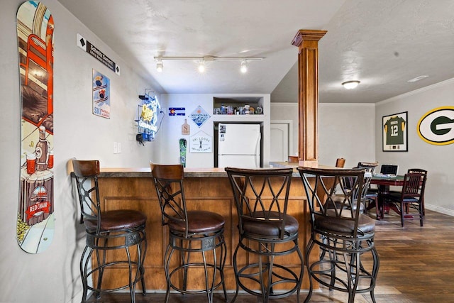 bar featuring bar, decorative columns, dark wood finished floors, baseboards, and freestanding refrigerator