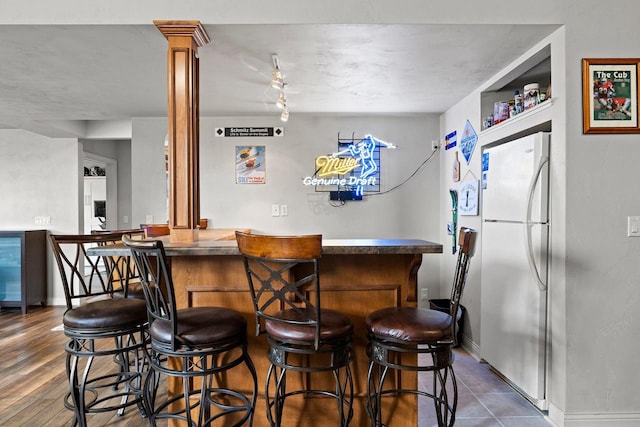 bar featuring baseboards, freestanding refrigerator, ornate columns, and a bar
