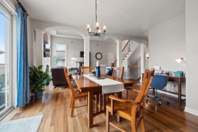 dining room featuring baseboards, ornate columns, arched walkways, and light wood-style flooring