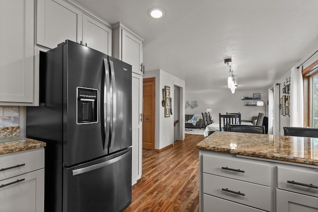 kitchen with light stone counters, open floor plan, dark wood-style flooring, and black refrigerator with ice dispenser