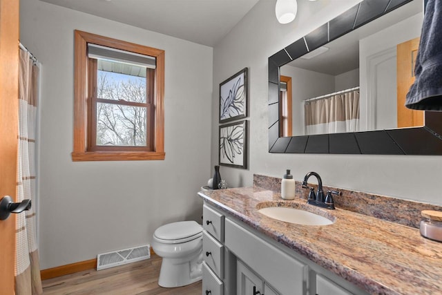 bathroom featuring vanity, toilet, baseboards, wood finished floors, and visible vents