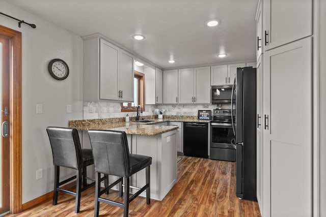 kitchen featuring a sink, a peninsula, wood finished floors, tasteful backsplash, and black appliances
