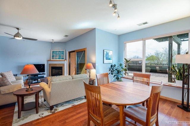 dining area featuring a glass covered fireplace, a ceiling fan, hardwood / wood-style floors, and visible vents