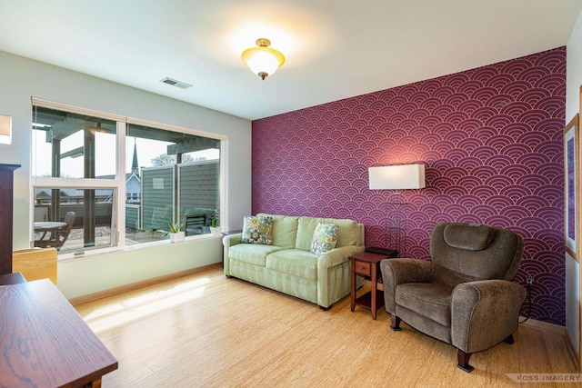 living room featuring visible vents, wood finished floors, an accent wall, baseboards, and wallpapered walls