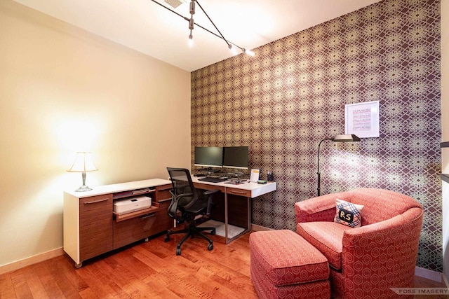 home office featuring track lighting, an accent wall, baseboards, wallpapered walls, and light wood-type flooring