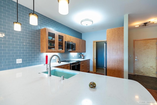 kitchen with brown cabinets, a sink, light countertops, stainless steel appliances, and glass insert cabinets
