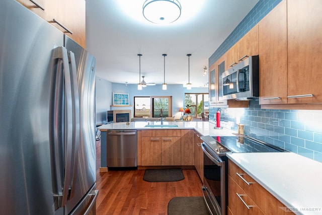 kitchen with brown cabinets, dark wood finished floors, a sink, a peninsula, and stainless steel appliances