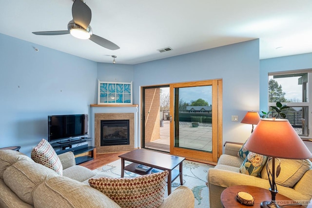 living room with a ceiling fan, a glass covered fireplace, wood finished floors, and visible vents