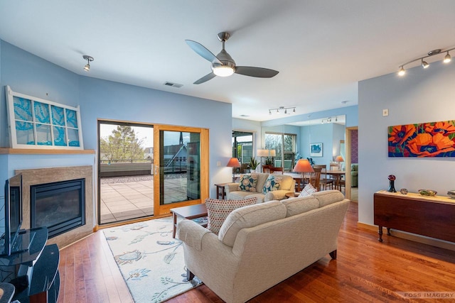 living room with rail lighting, visible vents, a glass covered fireplace, and wood finished floors