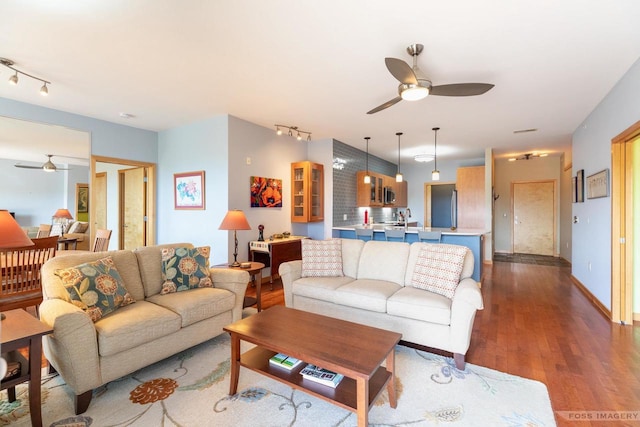 living area with baseboards, a ceiling fan, rail lighting, and wood finished floors